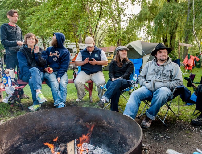 a group of people gathered in chairs around a campfire.