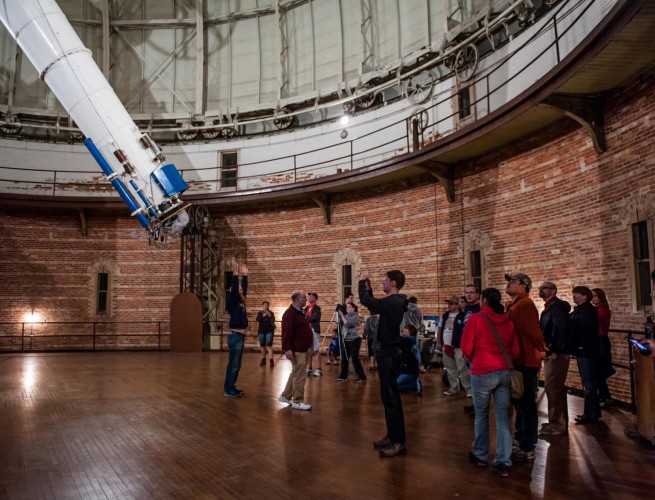 A group of people are led on a tour of the Yerkes Observatory, standing in the 40-inch dome.